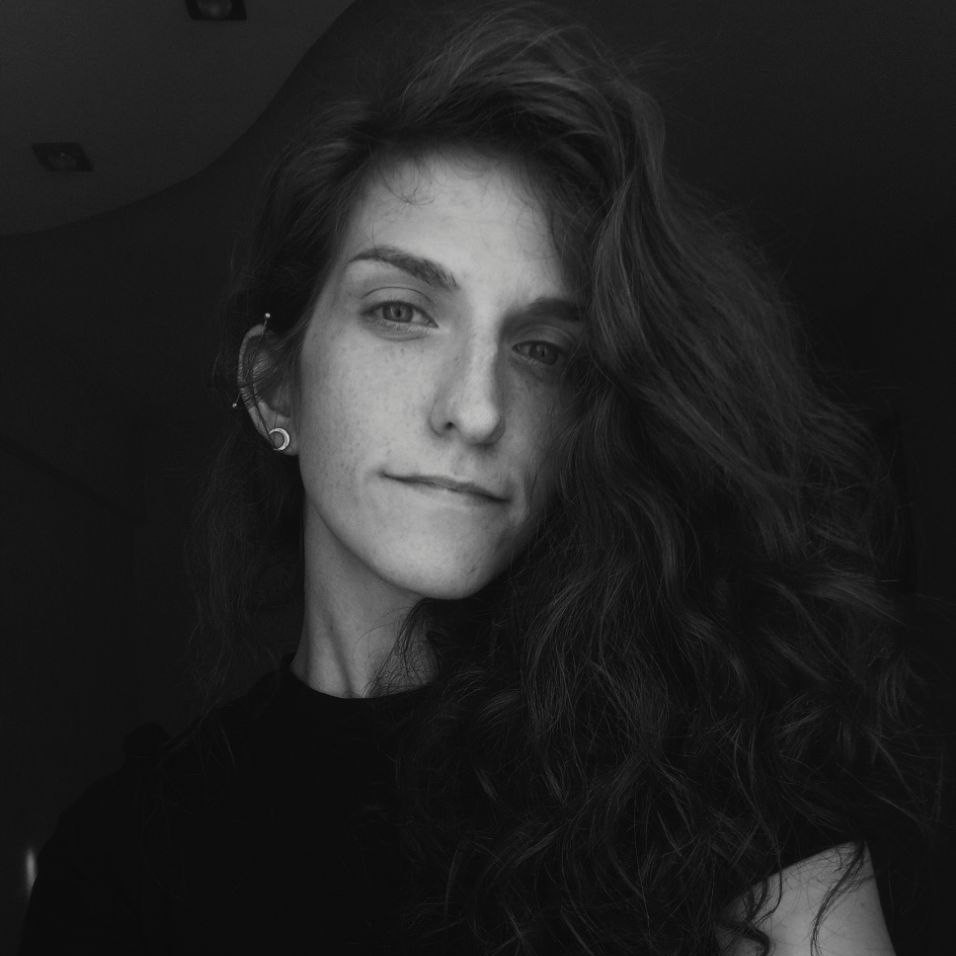 A black and white selfie of a woman with a curly hair and with bitch face wearing black t-shirt